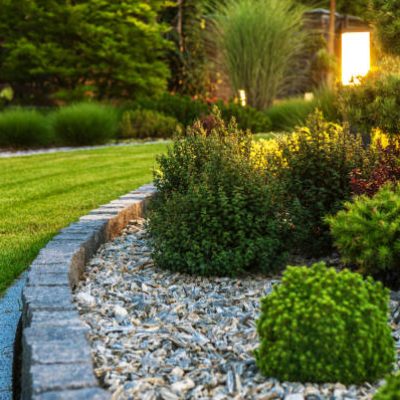 Closeup of Professionally Landscaped Flower Bed with Decorative Green Garden Plants and Evenly Mowed Lawn in the Background.