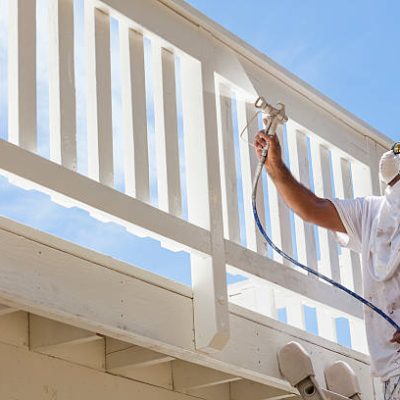 House Painter Wearing Facial Protection Spray Painting A Deck of A Home.